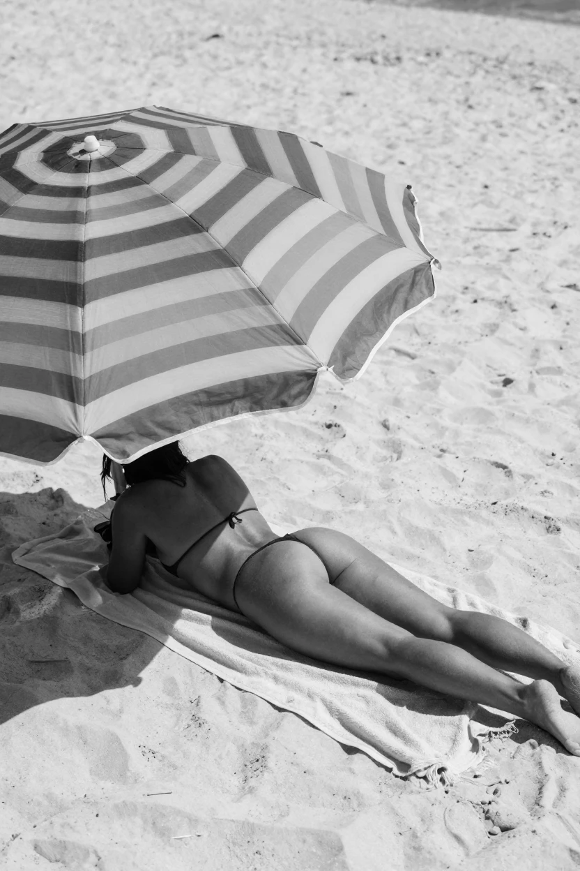 A sunbather relaxes beneath a colorful umbrella on a quiet stretch of white sand.